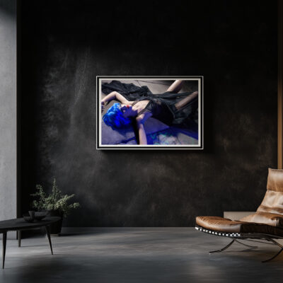 Modern art print of a woman with blue hair lying on the ground, framed and displayed on a dark wall in a contemporary living room with minimalist decor.